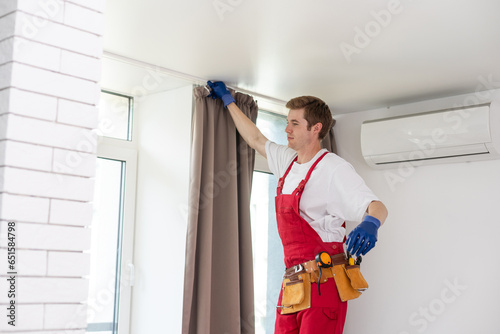 A male repairman installs a curtain rod and hangs curtains in the house. services to help with household chores and repairs