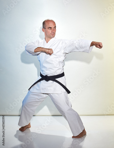 Adult athlete with black belt doing formal exercises on white background