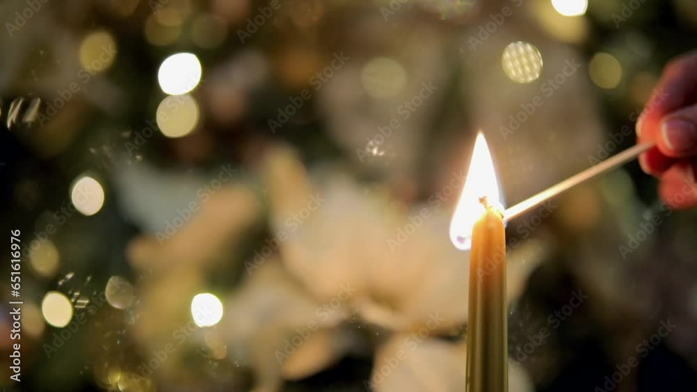 
Lighting the candle and Christmas tree branches with ornaments against bokeh background.