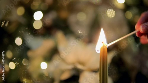 
Lighting the candle and Christmas tree branches with ornaments against bokeh background.