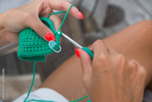 Closeup of a young Latina girl's hands crocheting with green yarn.
