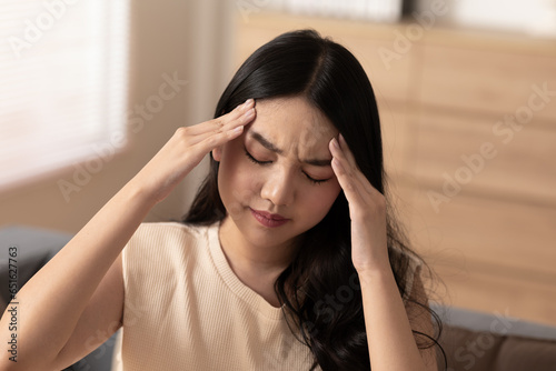 Asian young Woman has a Migraine and headache after wake up in cozy bedroom at home,Suddenly of painful attack on head massage around on pain spot,Healthcare Concept