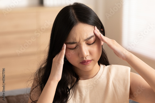 Asian young Woman has a Migraine and headache after wake up in cozy bedroom at home,Suddenly of painful attack on head massage around on pain spot,Healthcare Concept