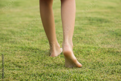 Children's feet are walking barefoot on the green grass. Self-massage on natural surfaces to correct curvature.