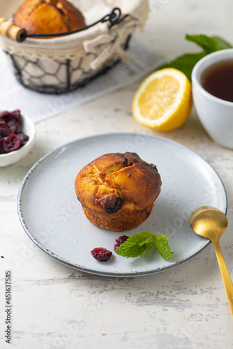 muffins with cranberries on grey plate with cup of tea, lemon and mint