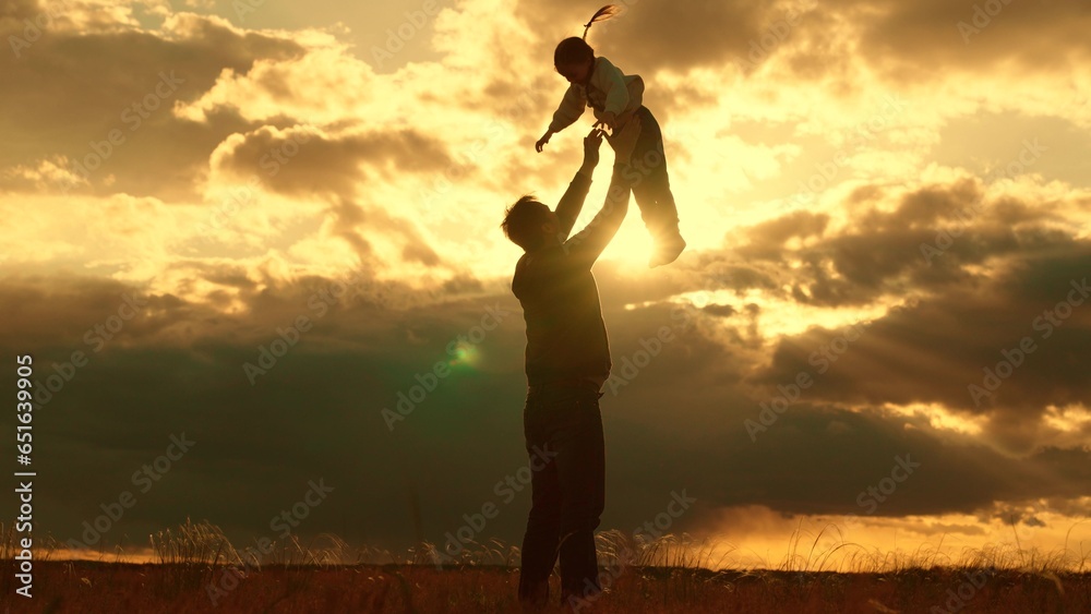 Concept, family safety trust, Dad plays with his daughter, throws child into sky with his hands, happy kid. Silhouette, Father of daughters playing together in park against backdrop of sun and clouds