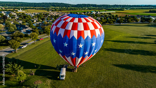 An Aerial View on a Stars and Stripes, Hot Air Balloon Floating Over a Countryside Community, on a Beautiful Summer Day © Greg Kelton
