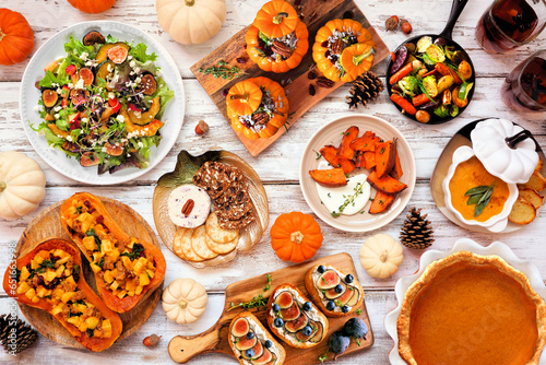 Delicious autumn meal table scene. Above view on a white wood background. Stuffed pumpkins and squash, sweet potatoes, appetizers, soup, vegetables and pumpkin pie. photo