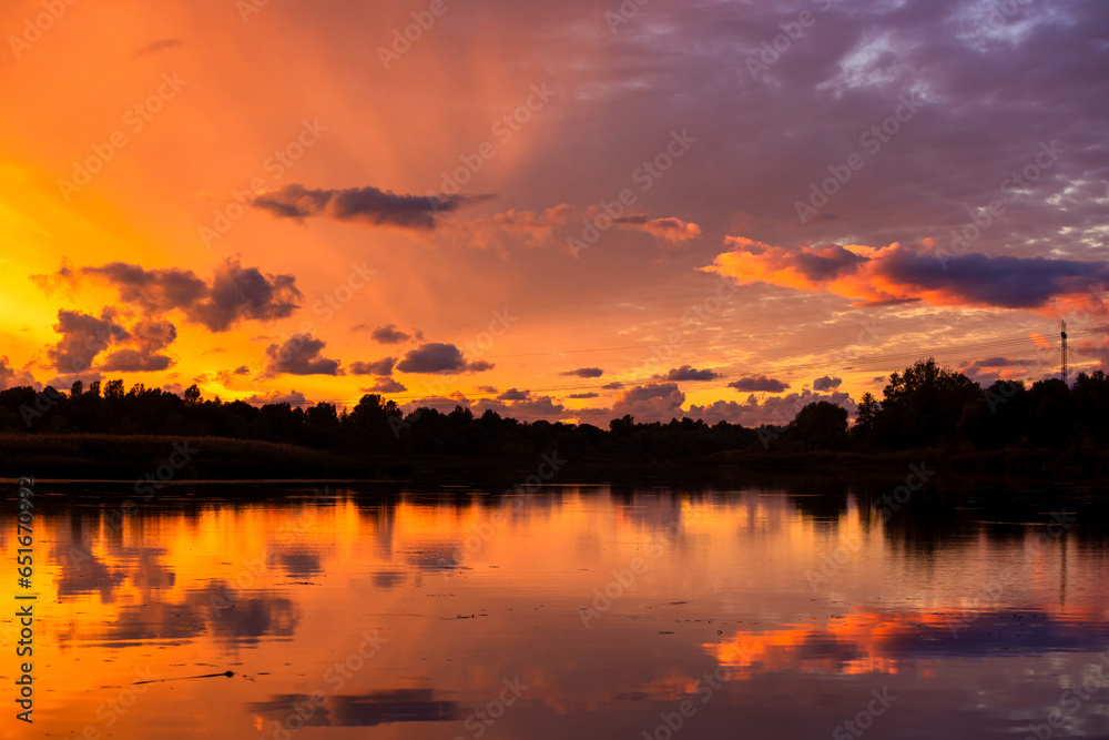 Amazing sunrise in rural scene. Symmetry of the sky in a lake at sunset. Clouds reflecting on the water. Quiet relaxing scene with a beautiful colorful cumulonimbus.