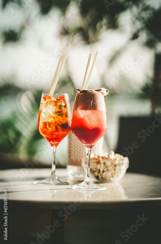 Two long glasses with orange cocktails made from red bermouth on a table next to a bowl of popcorn with an artistically blurred background