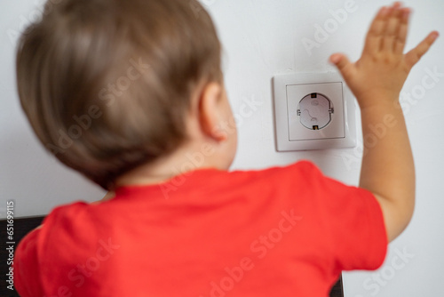 A child, a little boy, touches an electrical outlet with his hands. Danger! Childproof socket