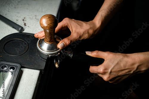 Coffee making process. Woman barista pressing groud coffee with tamper. Close up view. photo