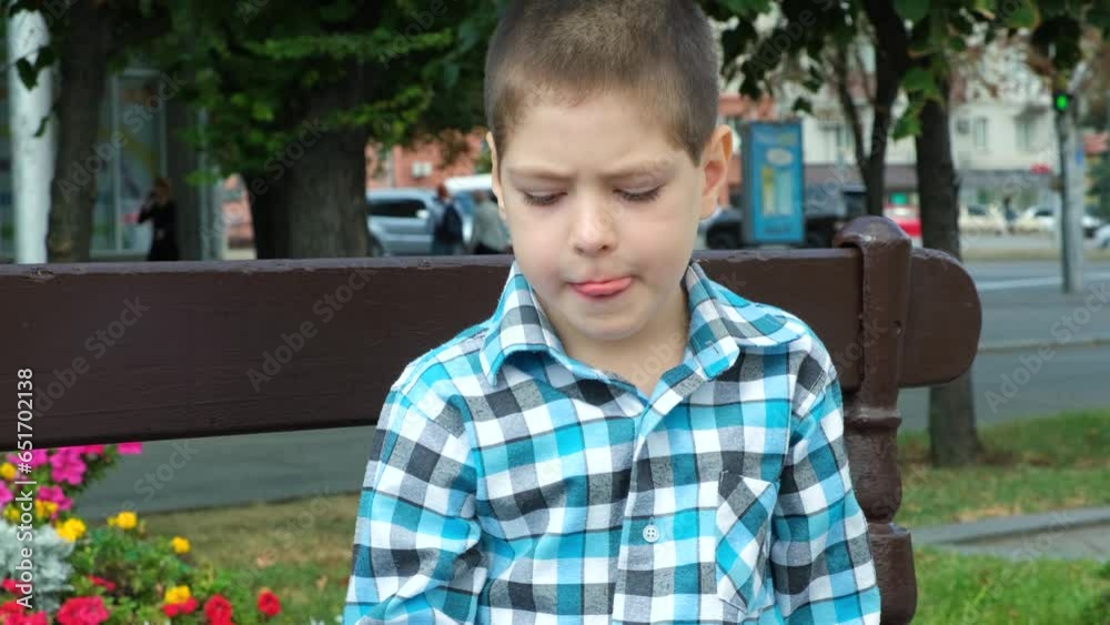 A little boy eats a lollipop while sitting on a bench in the city A little boy eats a lollipop while sitting on a bench in the city