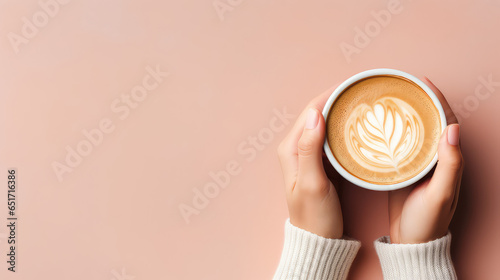 Top view of a female hands in a warm sweater holding mug of delicious cappuccino coffee. Pastel pink background with copy space, banner template.  photo