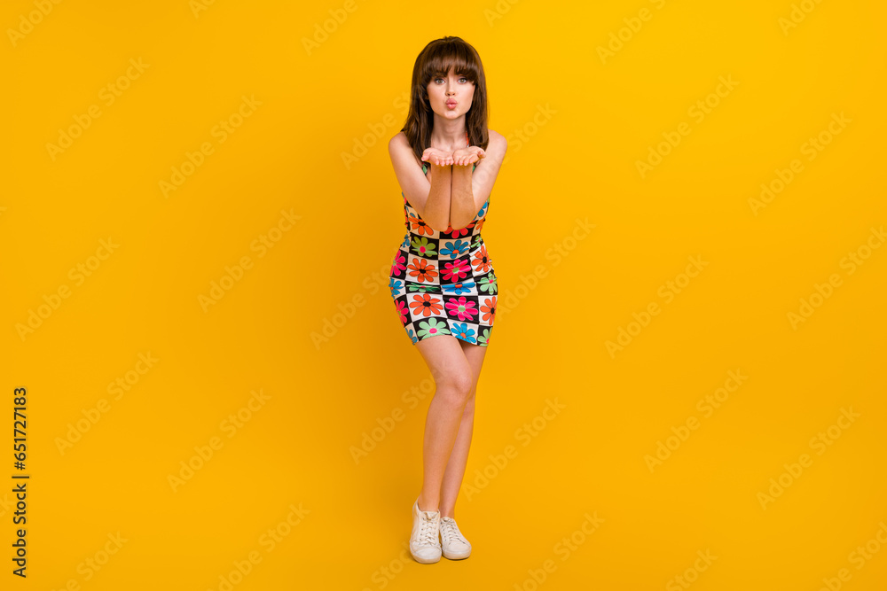Full length photo of positive flirty lady wear flower print clothes sending arms kiss isolated yellow color background Full length photo of positive flirty lady wear flower print clothes sending arms kiss isolated yellow color background