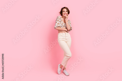 Full length photo of pleasant gorgeous adorable woman wear print top white pants hold finger on lips isolated on pink color background