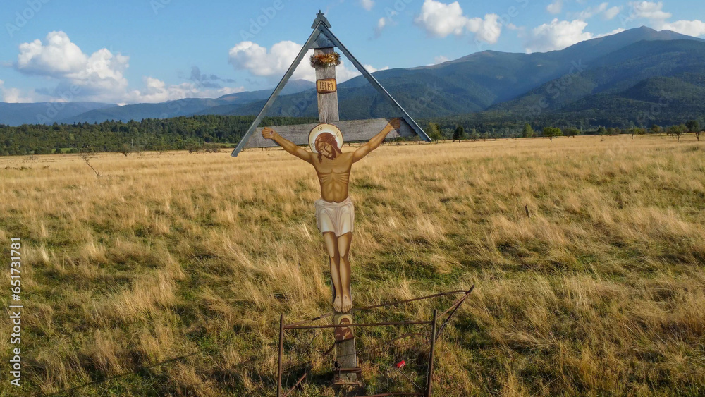 Christian orthodox cross in the meadow, on the side of a road. Traditional view in rural Romania, in the Carpathian mountains.