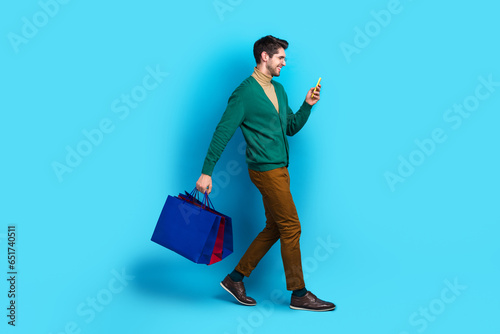 Full body photo of young working man brunet hair walking going with phone pre order adidas new collection isolated on blue color background photo