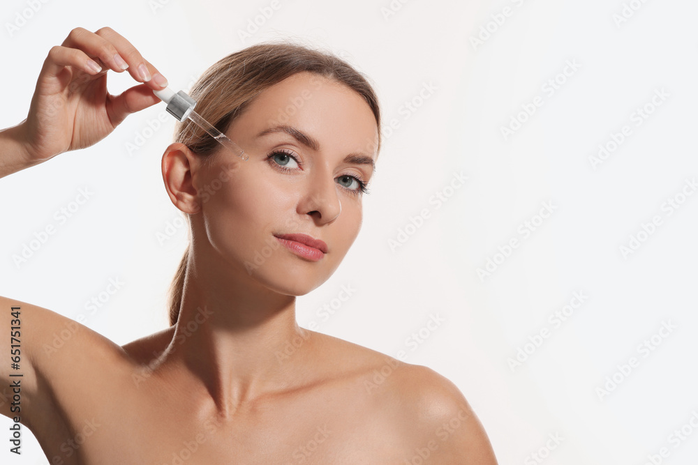 Beautiful woman applying cosmetic serum onto her face on white background, space for text