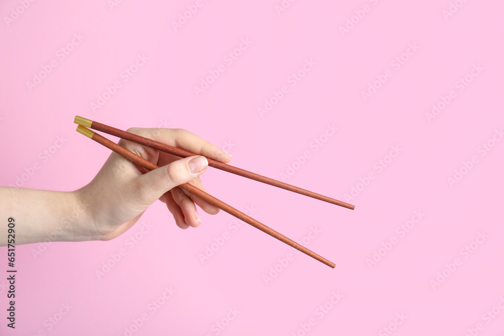 Woman holding pair of wooden chopsticks on pink background, closeup Woman holding pair of wooden chopsticks on pink background, closeup