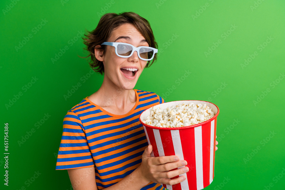 Photo portrait of attractive young woman hold popcorn bucket eating wear trendy striped clothes isolated on green color background Photo portrait of attractive young woman hold popcorn bucket eating wear trendy striped clothes isolated on green color background