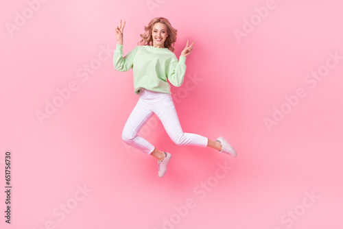 Full length portrait of excited active person jumping demonstrate v-sign empty space isolated on pink color background