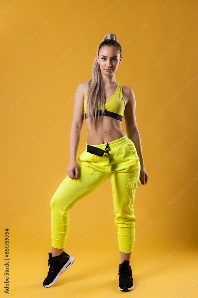 Beautiful girl in yellow outfit dancing zumba. Happy dance instructor against dark yellow or orange background.
