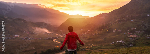 Young man traveler looking at beautiful landscape with mountains and green rice terraces view at sunset in Sapa, Vietnam © Kittiphan
