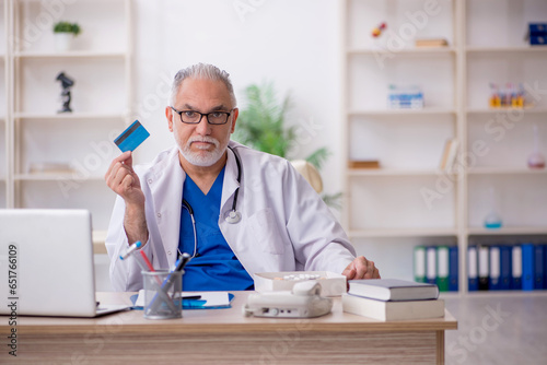 Old male doctor holding credit card