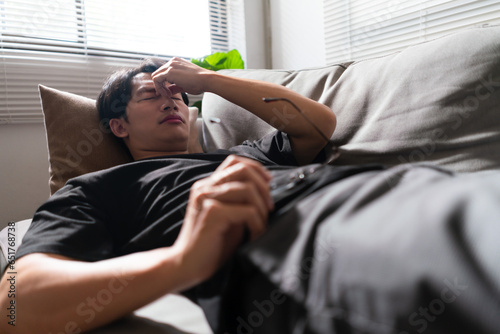 Man with mental health problem lying on the couch with exhausted and using hand to massage nose