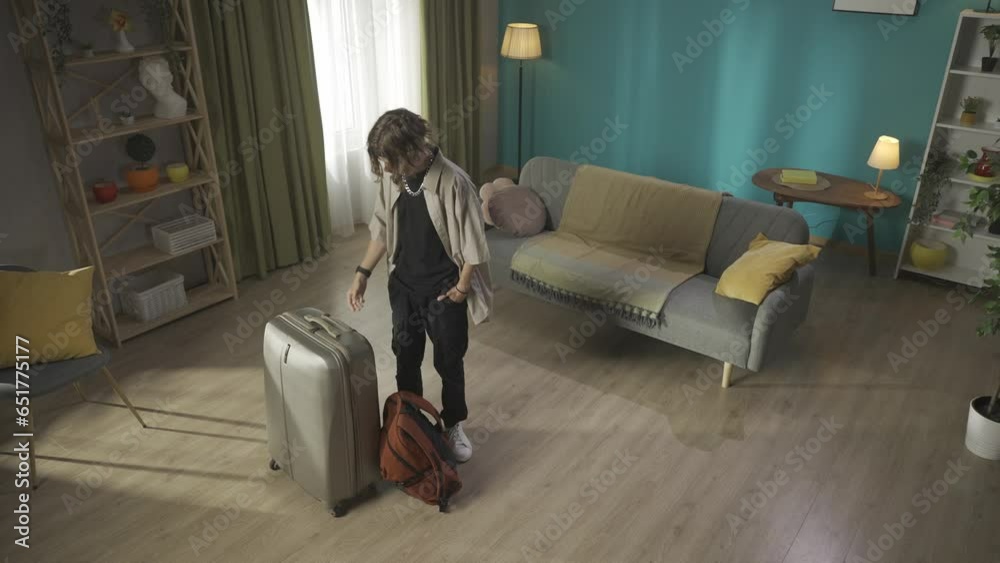 Video of a teenager, young man moving out. He is looking around to see ifhe forgot something. The boy takes his suitcase and goes out of the frame. HDR BT2020 HLG Material.