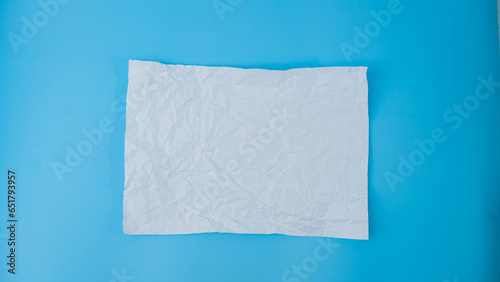 A paper ball is spread out into a blank sheet on blue background. Crumpled blank white paper with copy space for text or advertising space. © Some