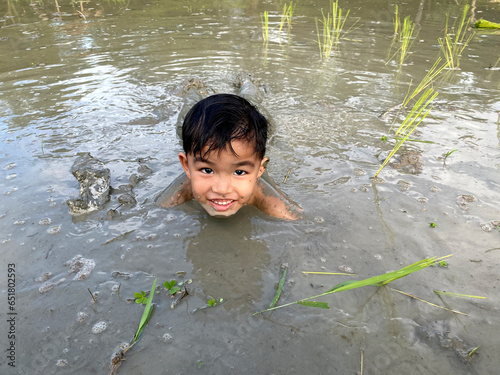 Thailand Asia boy is enjoy playing in the mud of rice field. Outdoor kid learning activity.