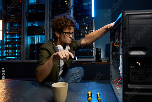 Young IT technician using flashlight to find problem with computer in modern data center photo