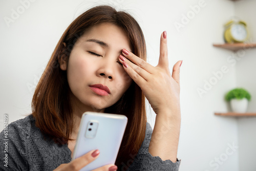 Asian woman suffering from eye pain from phone screen time cause of blue light photo