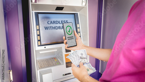Young woman using the smart phone for cardless withdrawing the cash near the ATM photo