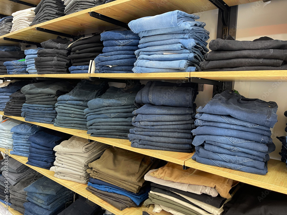 Many blue and black jeans in closet. Stack of jeans on shelf. Concept of buy, sell , shopping and denim fashion