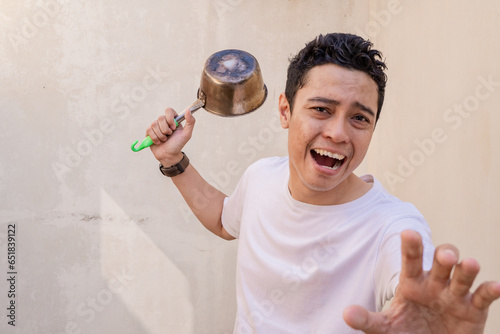 Indonesian men pose hitting hold the pan wear white tshirt. The photo is suitable to use for man expression advertising and fashion life style. photo