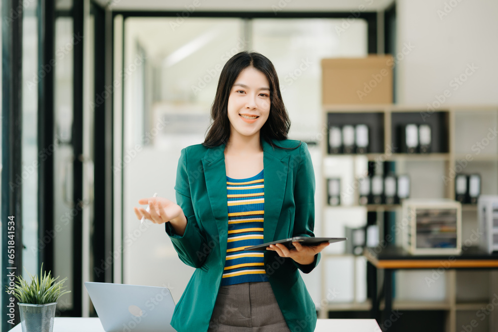 Confident Asian woman with a smile standing holding notepad and tablet at the office. Confident Asian woman with a smile standing holding notepad and tablet at the office.
