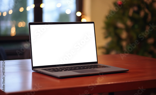 Laptop on desk with blank screen, Christmas tree and gifts in background, clipping path included. Festive home office.