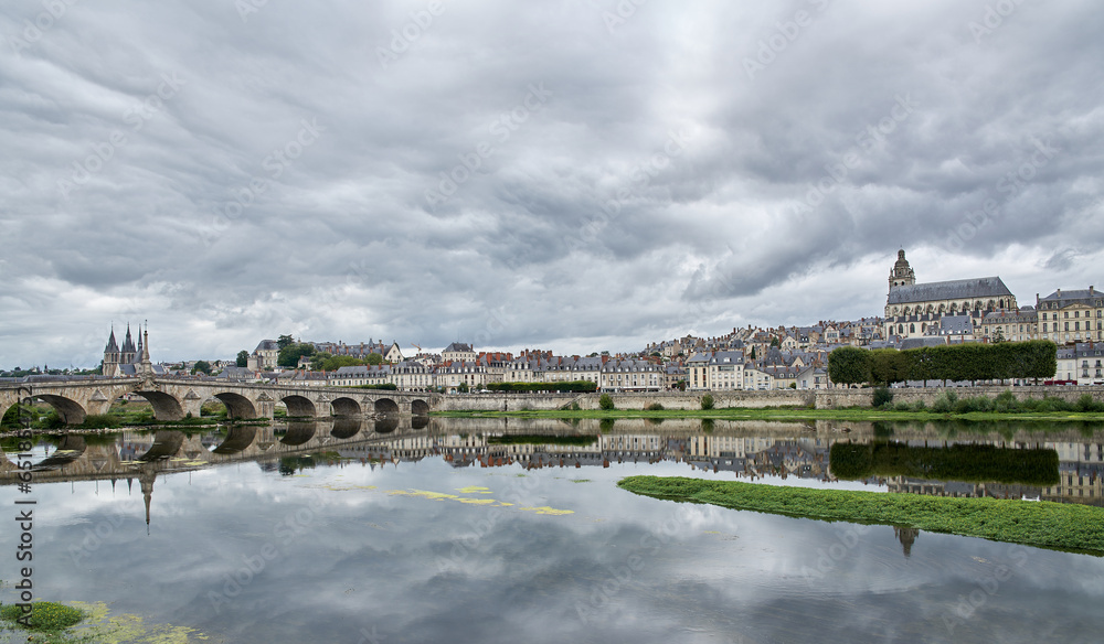 Fototapeta premium Skyline of a town with its cathedral, a river and the reflection of the bridge and the town on the waters of the river with a gray sky with many clouds