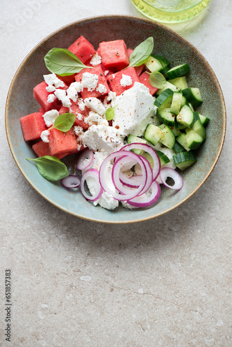 Plate with watermelon, feta and cucumber salad, vertical shot on a beige stone background with space, elevated view