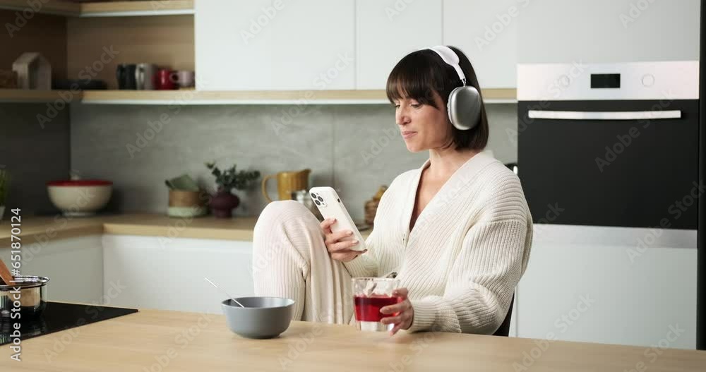 A delighted woman joyfully uses her phone in the kitchen while sipping on a beverage. Her happy demeanor and the refreshing drink contribute to a relaxed and enjoyable moment. A delighted woman joyfully uses her phone in the kitchen while sipping on a beverage. Her happy demeanor and the refreshing drink contribute to a relaxed and enjoyable moment.
