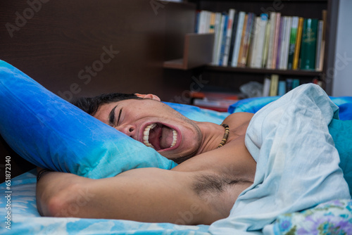 A man laying in bed with his mouth open, screaming because of a nightmare