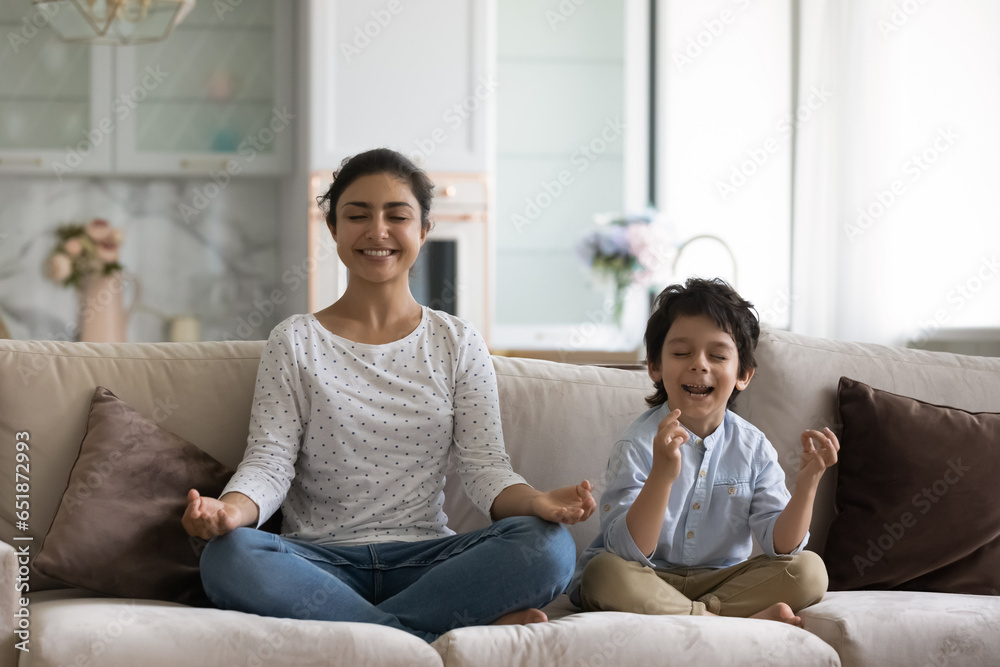 Smiling Indian mother with 5s son meditating on couch together, sitting in easy seat lotus, happy young mom teaching little boy child to practicing yoga, healthy lifestyle, enjoying leisure time Smiling Indian mother with 5s son meditating on couch together, sitting in easy seat lotus, happy young mom teaching little boy child to practicing yoga, healthy lifestyle, enjoying leisure time