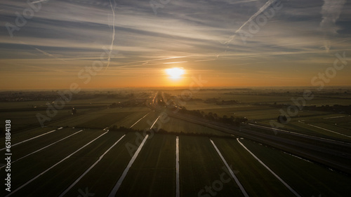 sun rises on arable farmland in green heart of Netherlands near Woerden. Drone photography picks up reflection in field drainage sluits
