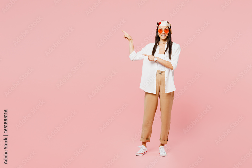 Full body young latin woman wear white shirt casual clothes sunglasses point index finger aside on area indicate on workspace area copy space mock up isolated on plain pastel light pink background. Full body young latin woman wear white shirt casual clothes sunglasses point index finger aside on area indicate on workspace area copy space mock up isolated on plain pastel light pink background.