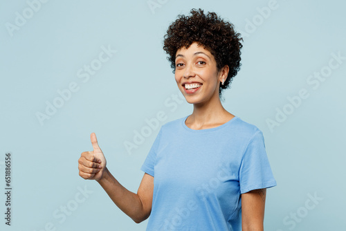 Side view young woman of African American ethnicity wears t-shirt casual clothes showing thumb up like gesture isolated on plain pastel light blue cyan background studio portrait. Lifestyle concept.