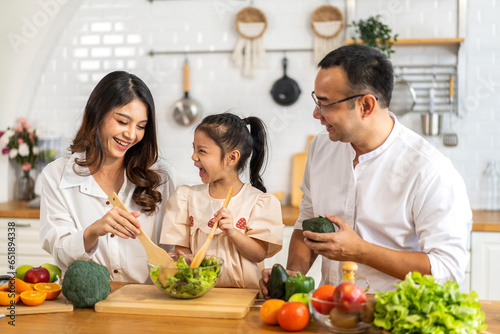 Portrait of enjoy happy love asian family father and mother with little asian girl daughter child having fun help cooking food healthy eat together with fresh vegetable salad and sandwich in kitchen