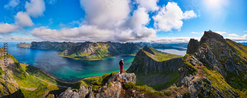 Hiker standing on the top of Husfjellet Mountain on Senja Island in northern Norway and enjoying spectacular views over surrounding fjords and mountains. photo